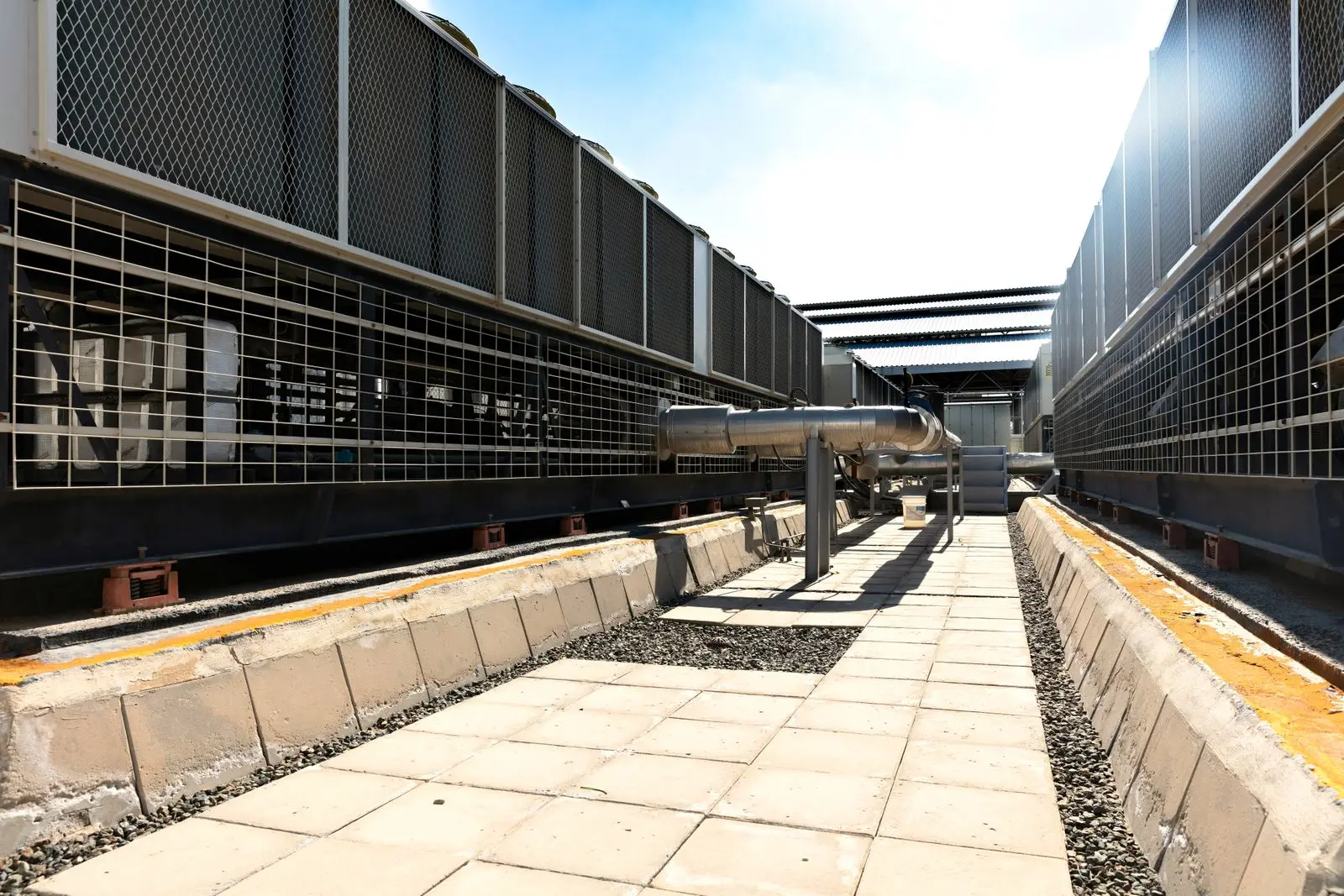 Banks of commercial rooftop air-cooled chiller units under a clear blue sky